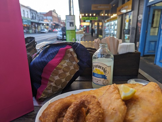A plate of fish and chips being eaten at a footpath table on a street in Collingwood 