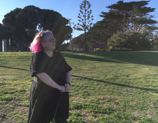 Person standing in a grassy area being thoughtful while holding a STICK