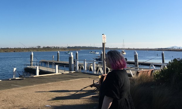 Person standing in the same spot as Hyunjin, with the marina visible behind them
