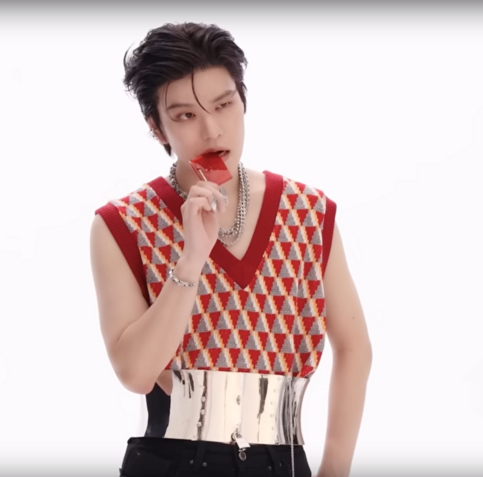 Seungmin in the locking chrome corset belt, during a photo shoot for ATE. His hair is swept back off his forehead, and he's holding a red candy up to his mouth