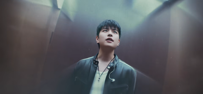 Seungmin sings in an elevator with a metallic wall behind him 